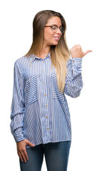 Poster - Beautiful young woman wearing elegant shirt and glasses smiling with happy face looking and pointing to the side with thumb up.