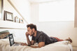 © Stefanie - Man at home lying in his bed working on his laptop.