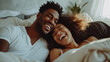 © Sasint - Interracial couple, laughing and relaxing on bed for morning bonding, funny relationship or joke at home.