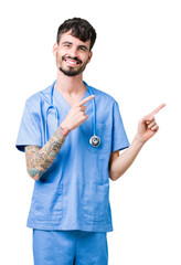 Canvas Print - Young handsome nurse man wearing surgeon uniform over isolated background smiling and looking at the camera pointing with two hands and fingers to the side.