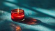 Red candle casting a warm glow on a textured blue background