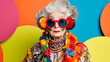 
Portrait of a gray-haired grandmother with bright makeup in colorful bright clothes and sunglasses posing against a bright studio background. The concept of beautiful aging, outrage, self-expression,