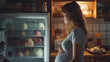 A hungry pregnant woman looks into the refrigerator at night.