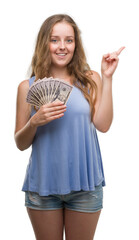 Wall Mural - Young blonde woman holding dollars very happy pointing with hand and finger to the side