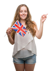 Wall Mural - Young blonde woman holding flag of UK very happy pointing with hand and finger to the side