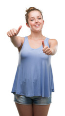 Wall Mural - Young blonde woman approving doing positive gesture with hand, thumbs up smiling and happy for success. Looking at the camera, winner gesture.