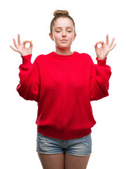 Wall Mural - Young blonde woman wearing bun and red sweater relax and smiling with eyes closed doing meditation gesture with fingers. Yoga concept.