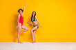 © deagreez - Full length photo of pretty cheerful girls dressed swimsuits dancing having fun empty space isolated yellow color background
