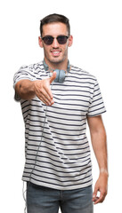 Wall Mural - Handsome young man wearing headphones smiling friendly offering handshake as greeting and welcoming. Successful business.