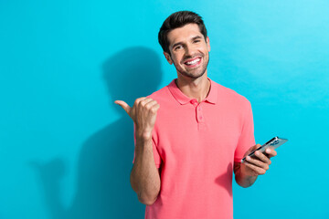 Poster - Photo of young guy recommend online casino for entertainment point finger mockup when using smartphone isolated on cyan color background