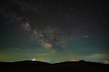 Milky way's core seen seen from the mountains, rising above a radio and gsm tower andcity pollution in a summer night. Horizon is lit in orange color. 