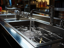 Chrome Faucets And Stainless Steel Sink, Two Large Bowls On A Metal Countertop In A Professional Kitchen In A Restaurant Or Cafe