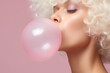 Blond woman blowing large bubblegum bubble in front of pink studio background