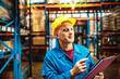 © Davor - Senior warehouse worker with hard hat checking inventory on clipboard