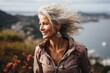 A fierce woman stands on a mountain, her wind-blown hair framing her determined face as she embraces nature and fashion with a flower in her hair and a stylish jacket