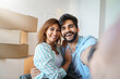 Young man and woman sitting on floor and taking selfie at new home. Splendid young smiling couple making selfie with boxes in background in new house.
