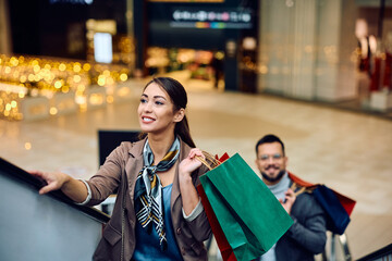 Sticker - Young woman goin up on escalator while shopping at  mall.