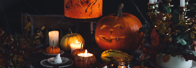 Elegant beautiful Halloween party table decor. Burning candled in vintage chandelier, handmade cake, meringue ghosts, handmade jack-o-lantern. Dark background wooden old furniture, spider web banner