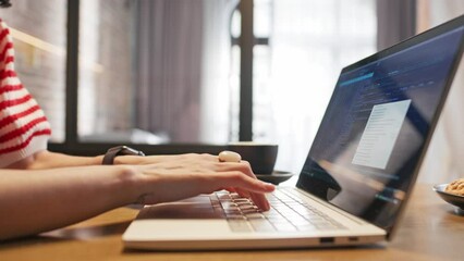 Side view of woman's hands with jewelry typing code on laptop. On screen visible programing software. Programmer female creating site or app. Working remotely in her cozy apartment.