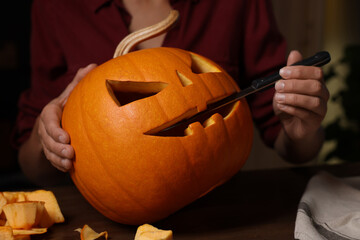 Wall Mural - Woman carving pumpkin for Halloween at wooden table, closeup