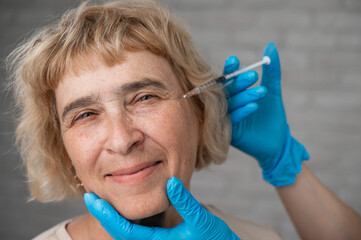 Wall Mural - The doctor makes beauty injections in the face of an old caucasian woman. Wrinkles around the eyes. 