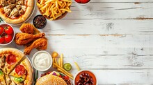 Junk Food Top Border. Pizza, Hamburgers, Chicken Wings And Salty Snacks. Above View Over A White Wood Banner Background