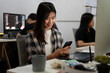 © bongkarn - Beautiful Asian female graphic designer is in the office, using her smartphone at her office desk.