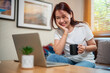 © nichapa - Young woman using laptop comfortably at home