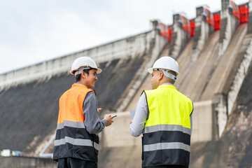 Wall Mural - Confident asian two maintenance engineers man inspection discussstion with tablet at construction site dam with hydroelectric power plant and irrigation. Team engineer man working at project