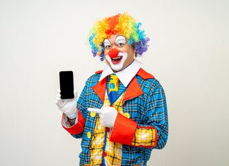 Wall Mural - Mr Clown. Portrait of Funny face Clown man in colorful uniform standing holding smartphone. Happy expression male bozo in various pose with cellphone on isolated background.