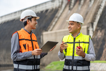 Wall Mural - Confident asian two maintenance engineers man inspection discussstion with tablet at construction site dam with hydroelectric power plant and irrigation. Team engineer man working at project