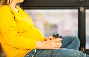 Wall Mural - Young pregnant woman sitting near window with coffee