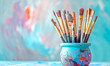 Art brushes in paint in a creative pot on a blue background with space for copy and text.
