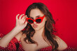 Stylish attractive young woman posing in red tight-fitting dress and in cat eye glasses
