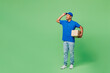 Full body delivery guy employee man wears blue cap t-shirt uniform workwear work as dealer courier hold blank cardboard box package look aside area isolated on plain green background. Service concept.