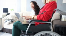 Portrait of friends spend time at home, watching movie and laughing, woman in wheelchair with laptop on lap. Disabled people, sisterhood, pastime concept