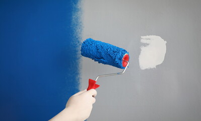 Wall Mural - Close-up of worker with roller tool ready to paint walls, cover in blue colour. Wall with part white and blue lac. Renovation, design, redecoration concept