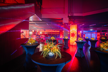  cocktail tables with floral centerpieces in a venue with dynamic red lighting and futuristic visual displays.