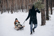 © Ananass - a man with a Christmas tree in his hands drives a sled with his daughters in the middle of a snowy forest