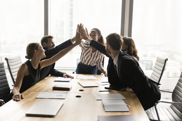 Wall Mural - Excited diverse group of colleagues celebrating teamwork success, job achievement, successful cooperation, partnership, profit, giving group high five over meeting table