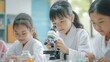 Young Asian kids wearing white scientist gown and using microscope while study and learning in science classroom with teacher. Young children education concept by experiment, fun and enjoy class.