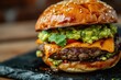 Closeup of a multilayer cheddar cheese and guacamole burger in a black dish with a wooden background