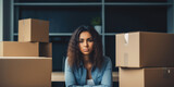 Fototapeta  - Portrait of a displeased young woman sitting among cardboard boxes, possibly during an office move or a job change.