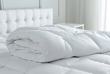 Close Up Of White Folded Duvet Lying On The Bed In Background Of A Modern Bedroom.