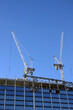 Two hoisting tower crane on the roof of being construction of modern high skyscraper  building against blue cloudless sky