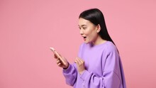 Young woman of Asian ethnicity wear purple sweatshirt hold use mobile cell phone typing browsing swipe chat send sms shopping online order delivery to home book tour isolated on plain pink background