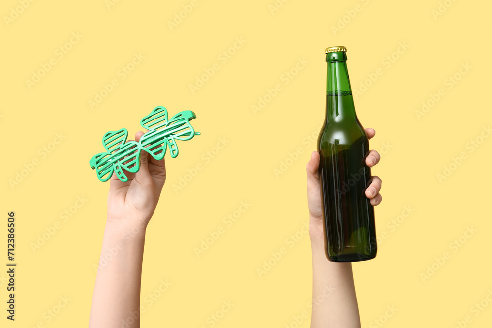 Hands with beer and party glasses on yellow background. St. Patrick's Day celebration
