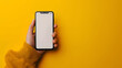 © Chaman - Hand holding the black smartphone with blank screen and yellow background, generative ai