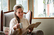 Mujer leyendo un libro mientras toma una taza de café, cómodamente en su sala de estar