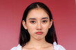 Portrait of a disappointed young asian woman with a subtle pouting expression, set against a vibrant red background.